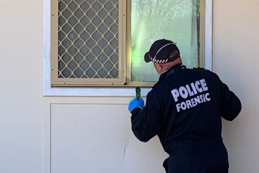A photo of the back of a forensics police officer next to a window.