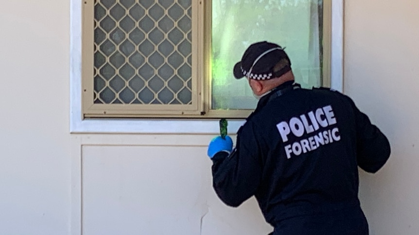 A photo of the back of a forensics police officer next to a window.