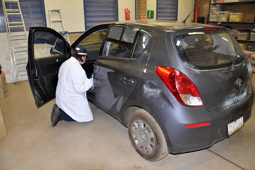 A police officer examines the grey Hyundai i20 car that was driven by the alleged offender.