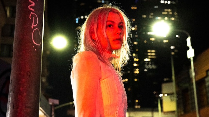 Phoebe Bridgers stands on a street corner at night