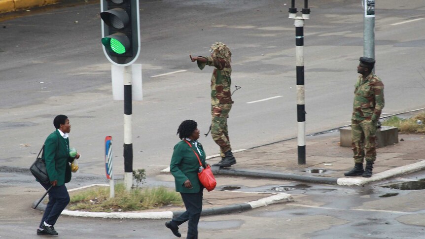 Armed soldiers stand on the road leading to President Robert Mugabe's office, as school children walk past.