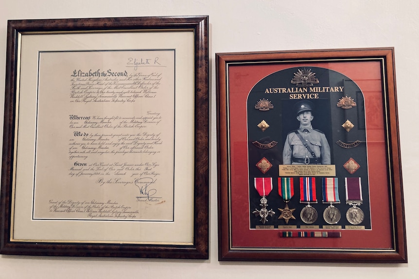 A photo of a framed citation signed by Queen Elizabeth II, next to another frame with military medals on display