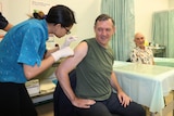 Northern Territory Chief Minister Michael Gunner smiles as he receives a coronavirus vaccine with his sleeves rolled up.