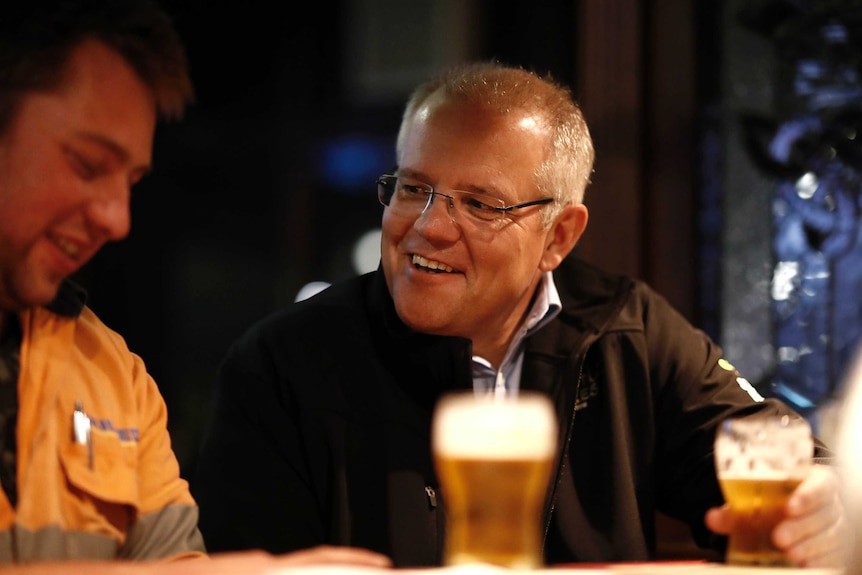 Scott Morrison, with a beer in his hand, smiles at a man sitting next to him at the bar.