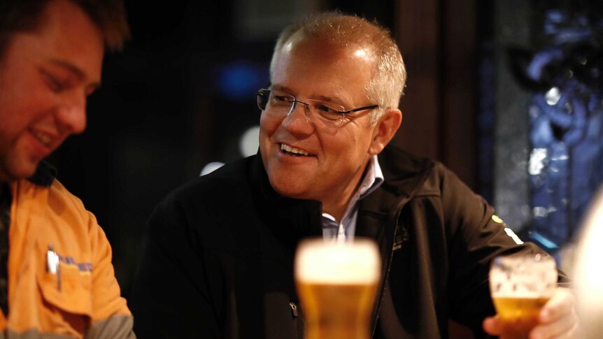 Scott Morrison, with a beer in his hand, smiles at a man sitting next to him at the bar.