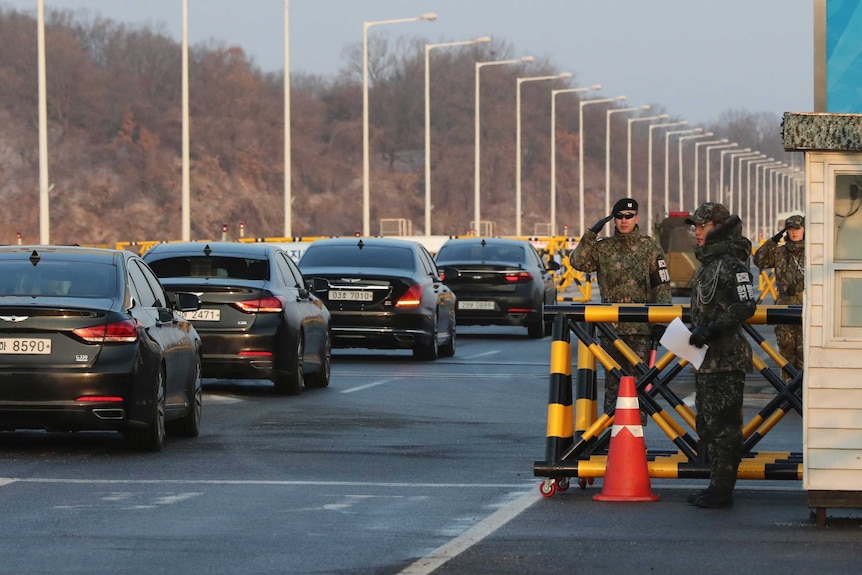 South Korean soldiers salute as vehicles carrying the South Korea's delegation. They are riding in black sedans.