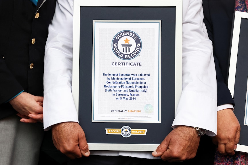A baker carries the Guinness World Records certificate for the longest baguette.