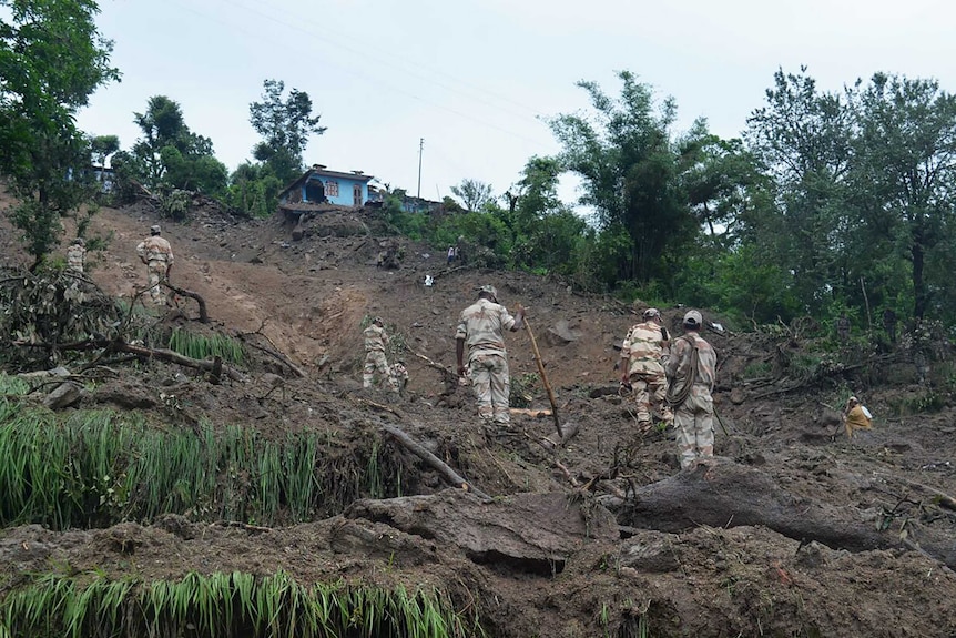 Indian soldiers search for survivors of a landslide on the side of a hill.