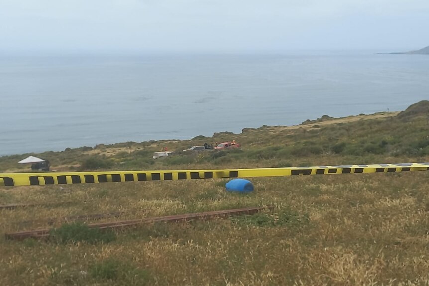 A yellow police tape above the ground on the side of a mountain with items on the grass area