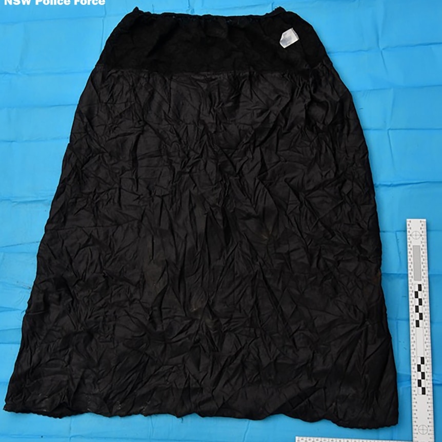 A heavily-crinkled black skirt laid on a blue sheet of plastic with a ruler placed against it. A NSW Police Force logo features