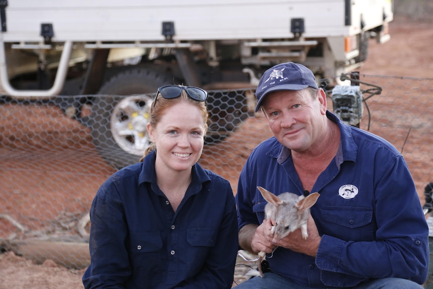 A woman and a man crouch holding a biby in the outback.