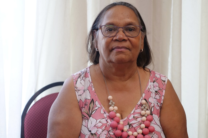 A First Nations woman wearing a pink top and necklace sits on a red chair in a meeting room.