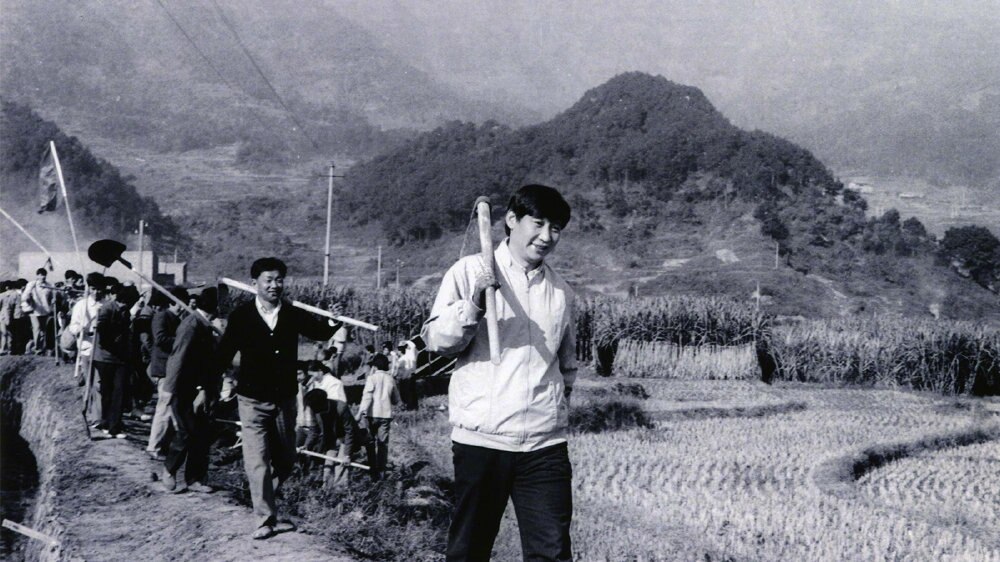 A black and white photo of Xi Jinping carrying a tool in the countryside.