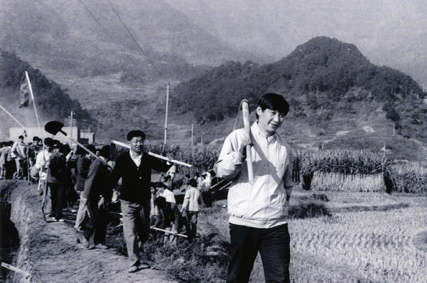 A black and white photo of Xi Jinping carrying a tool in the countryside.