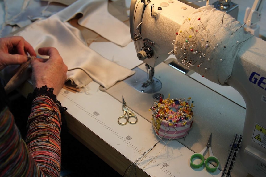 Woman's hands at sewing machine, with pincushion and scissors