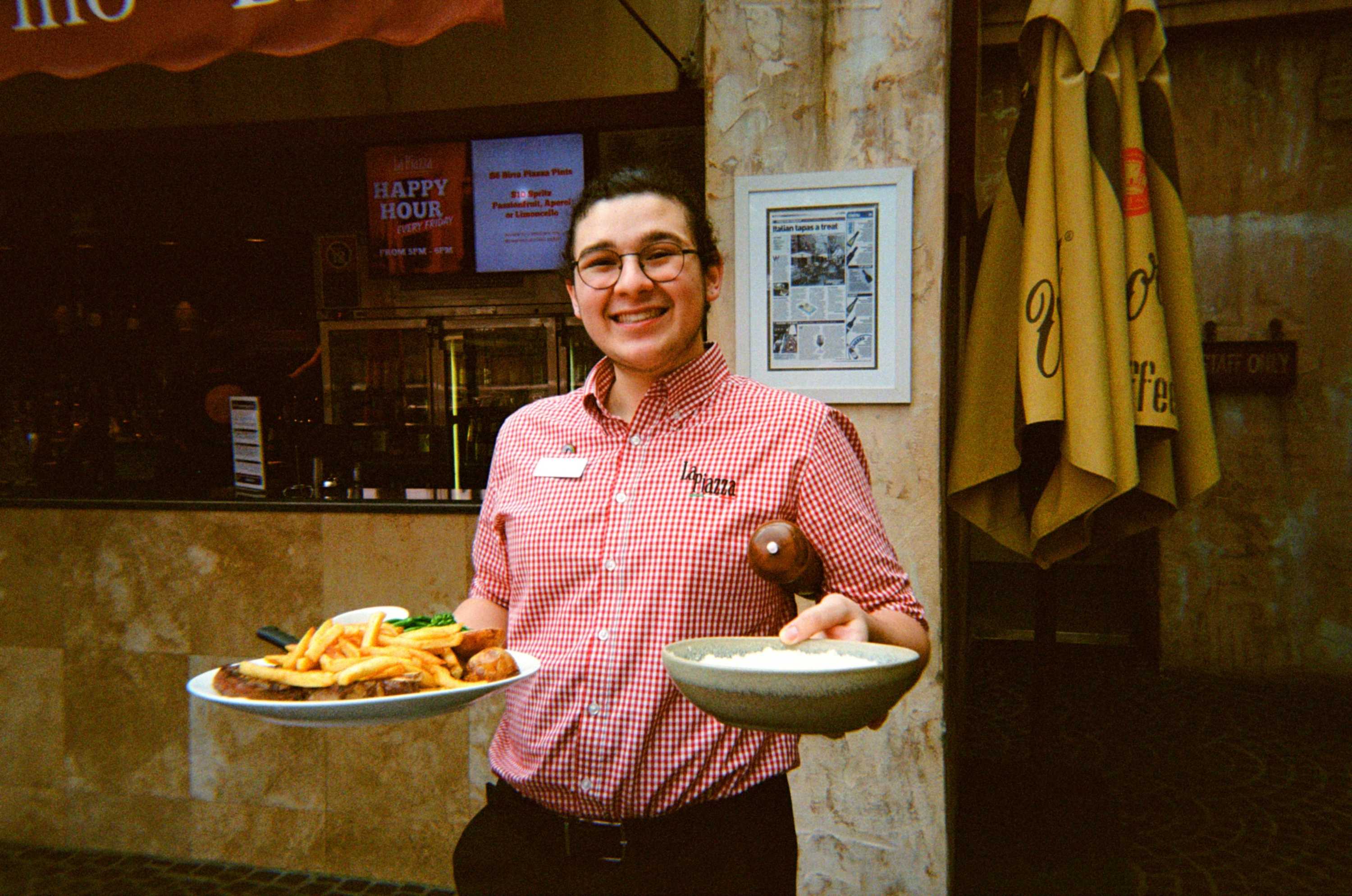 A young man with a ponytail holds two plates of food in a restaurant