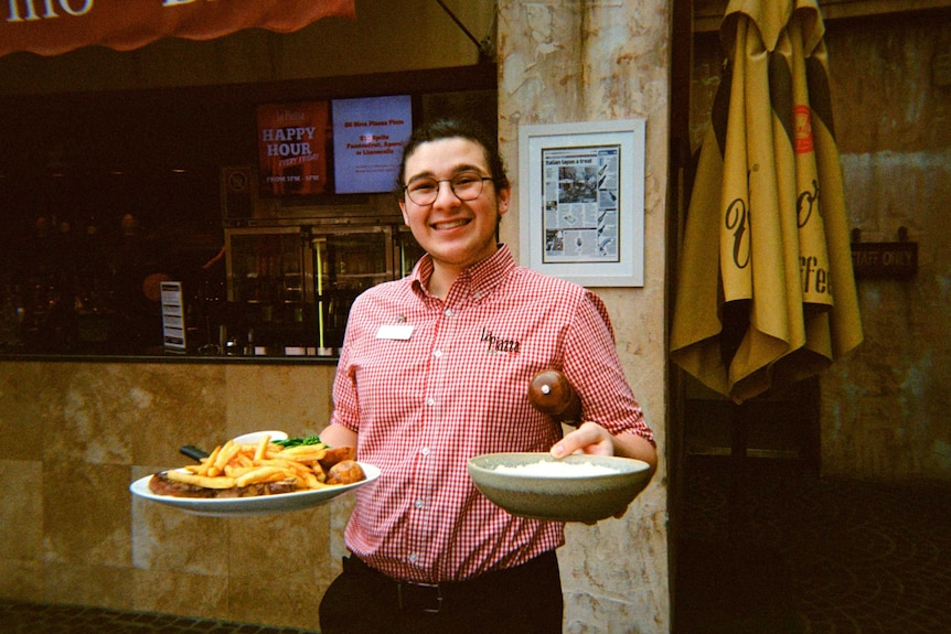 A young man with a ponytail holds two plates of food in a restaurant