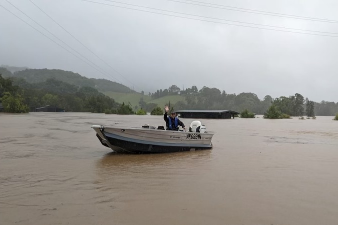 A tinnie is in the middle of a muddy river surrunded by hills and greenery and an overcast sky.