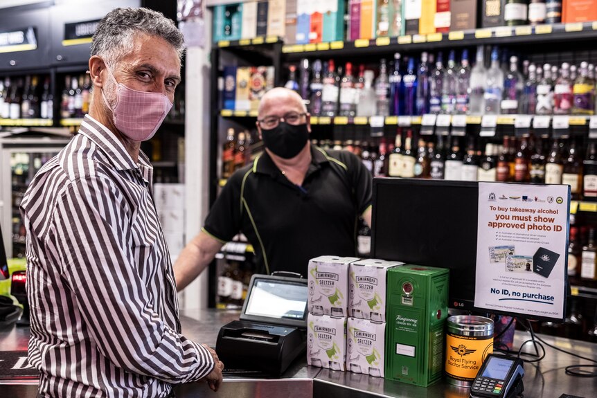 A man behind the counter at a liquor store serving a customer.  