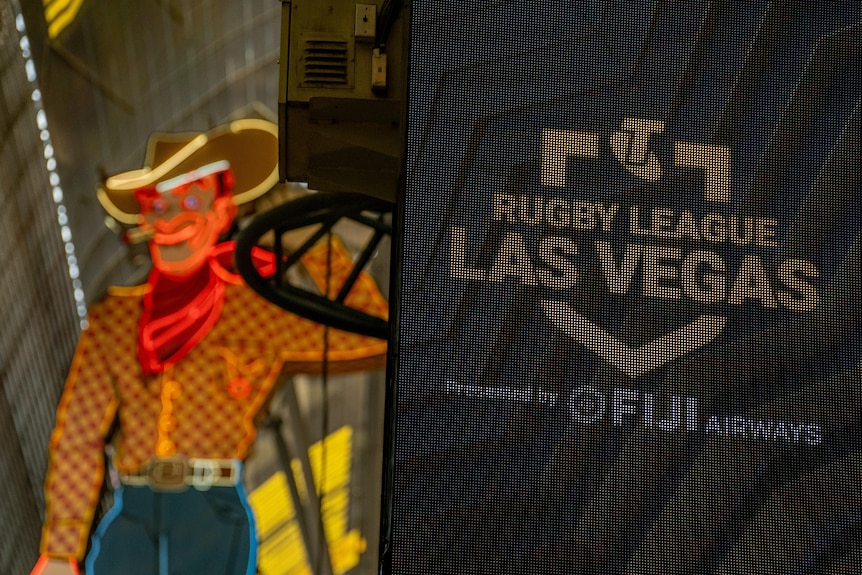 A sign for the NRL is seen with a lit up cowboy in the background.