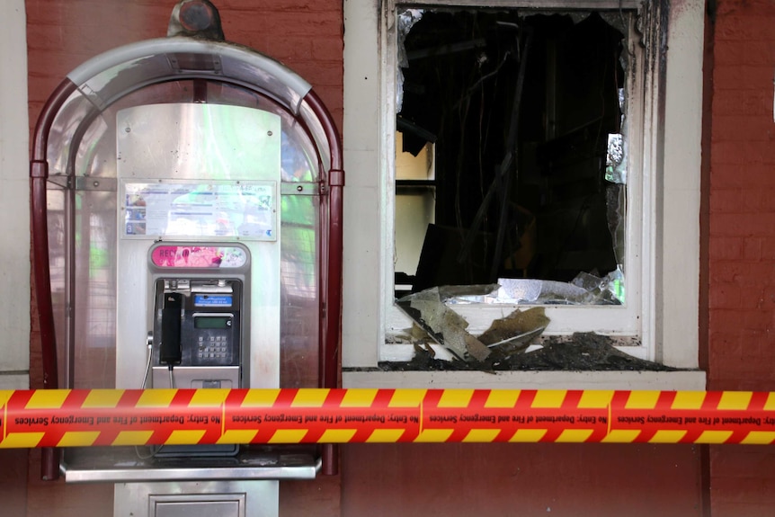 A broken window next to a phone booth at Perth Train Station with red and yellow tape barricading the scene.