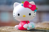 A plastic hello kitty toy sitting on a stone wall.