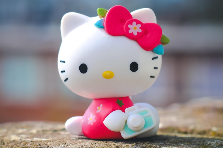 A plastic hello kitty toy sitting on a stone wall.