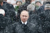 Vladimir Putin stands in the snow.