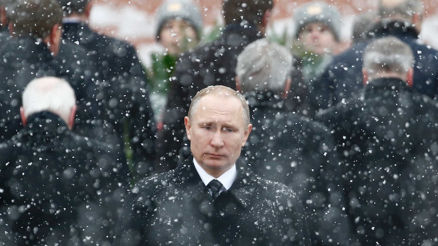 Vladimir Putin stands in the snow.