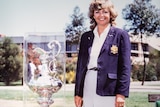 A smiling woman in a blazer poses with a large trophy.
