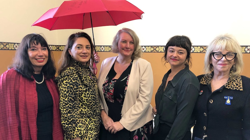 Five women standing with one holding a red umbrella