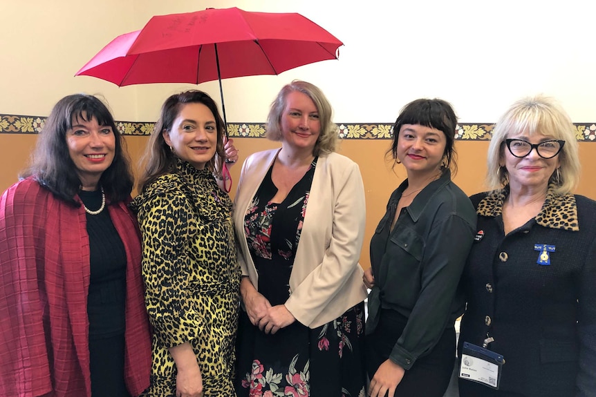 Five women standing with one holding a red umbrella