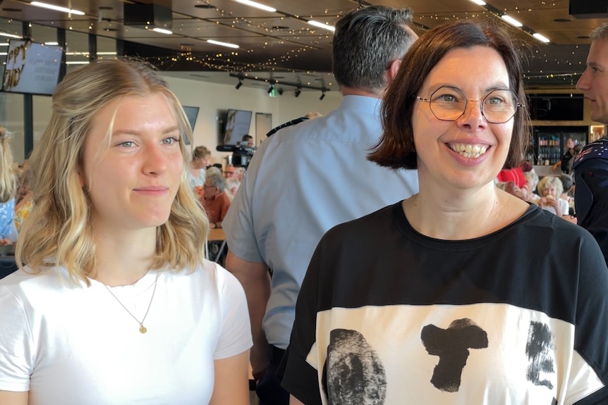 Two fair-skinned women, young Sylvia with blonde curls in white shirt, and Rebecca with brunette bob and glasses.