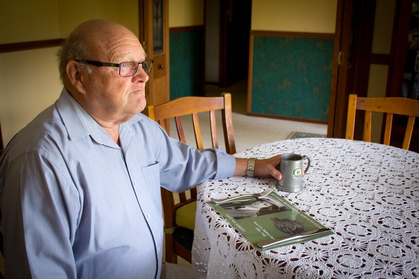 Ray Hartigan sits at a table with a placemat memorial set in front of him.