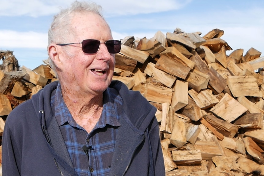 He stands by a pile of wood and laughs