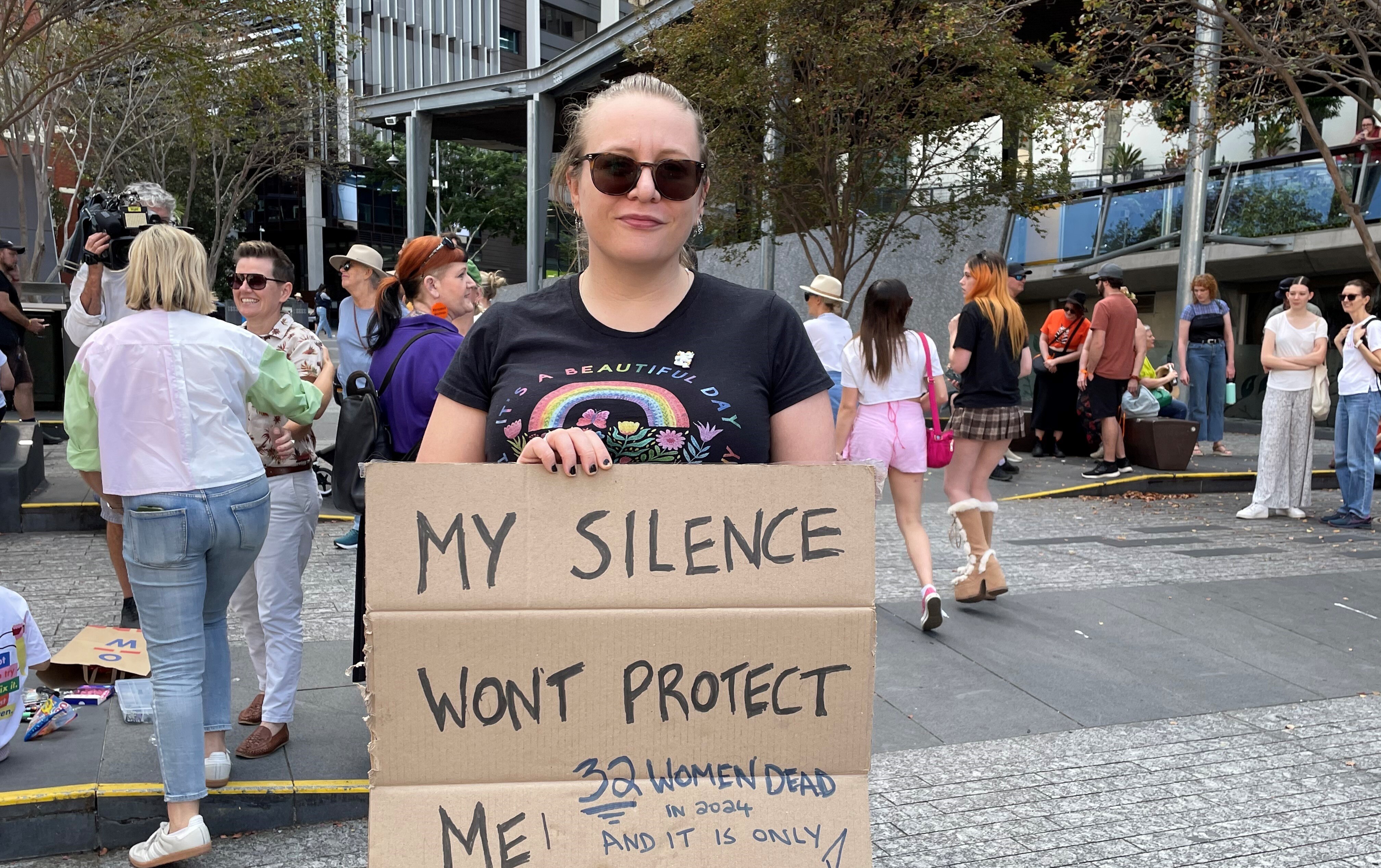 A woman stands holding a sign that says, my silence won't protect me. 