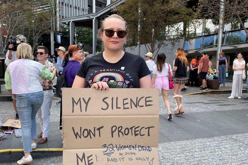 A woman stands holding a sign that says, my silence won't protect me. 