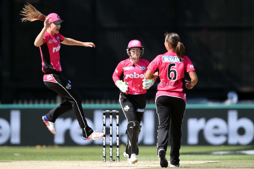 Three Sydney Sixers players celebrate on the field.