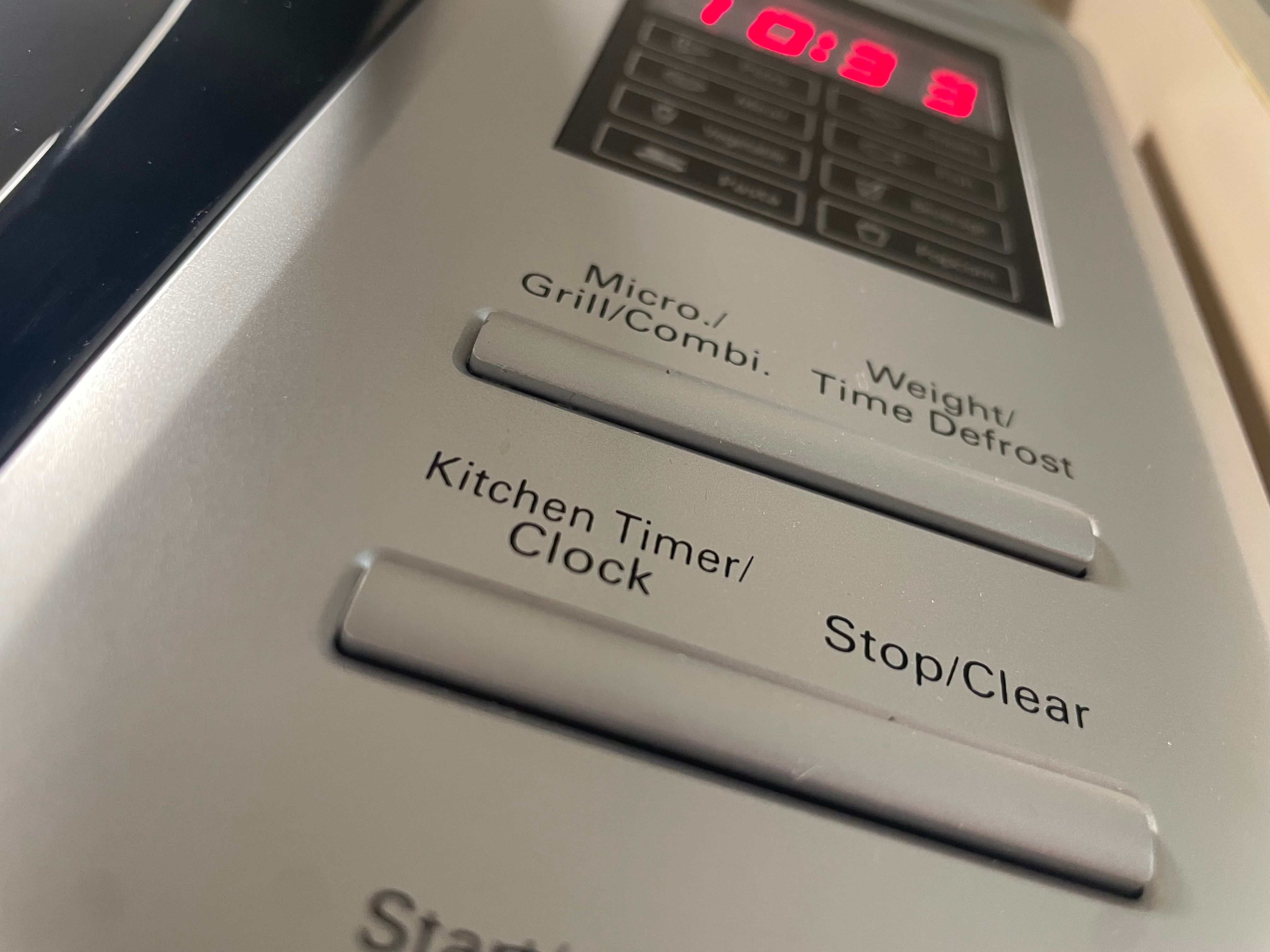 The buttons on a microwave panel, focusing on the clock-setting button