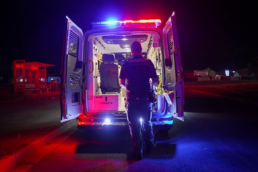 A paramedic looking inside an open ambulance, which has its lights on
