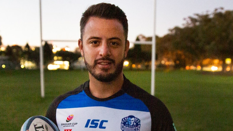 A man wearing a jersey and carrying a football stands in front of a goal.