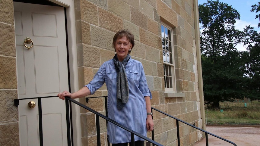 A woman stands outside a sandstone building
