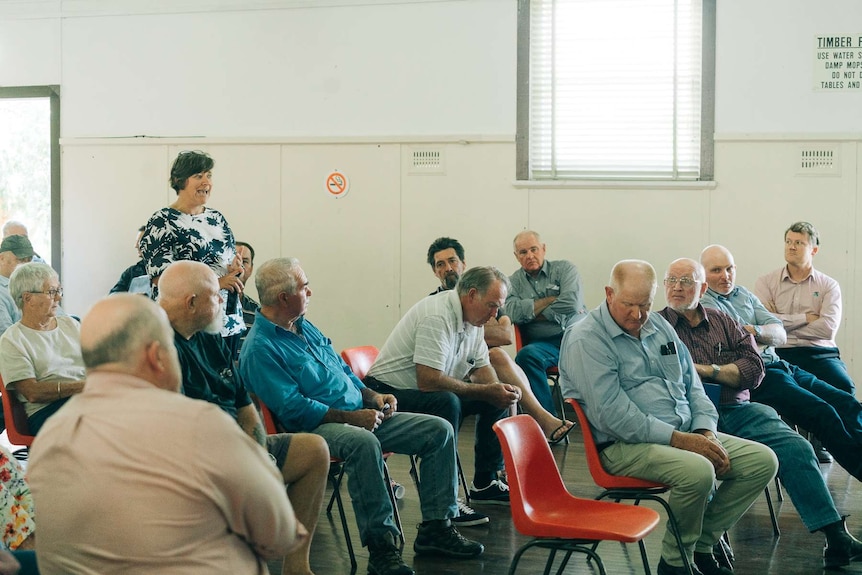 A woman standing and speaking with others sitting listening.