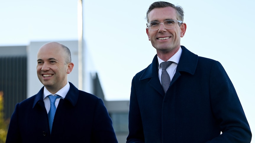 two men smiling standing next to each other and one wearing glasses