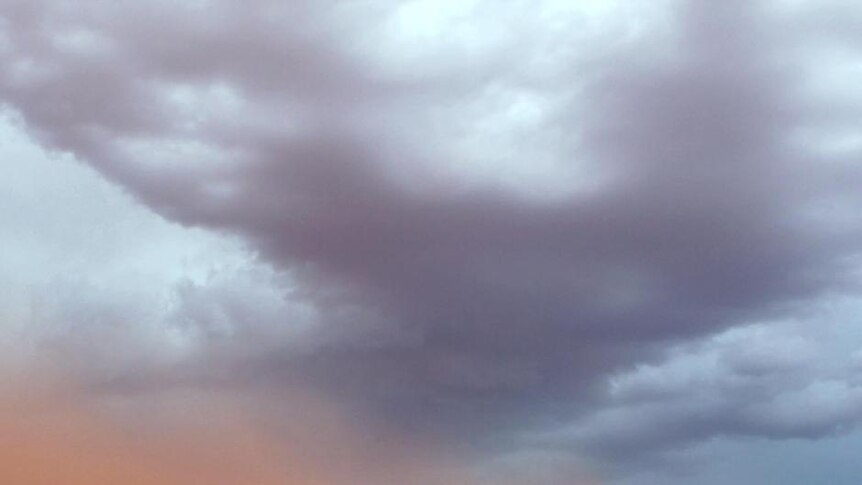 A red dust cloud blows across the bare earth of mining town Coober Pedy as dark clouds gather