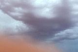 A red dust cloud blows across the bare earth of mining town Coober Pedy as dark clouds gather