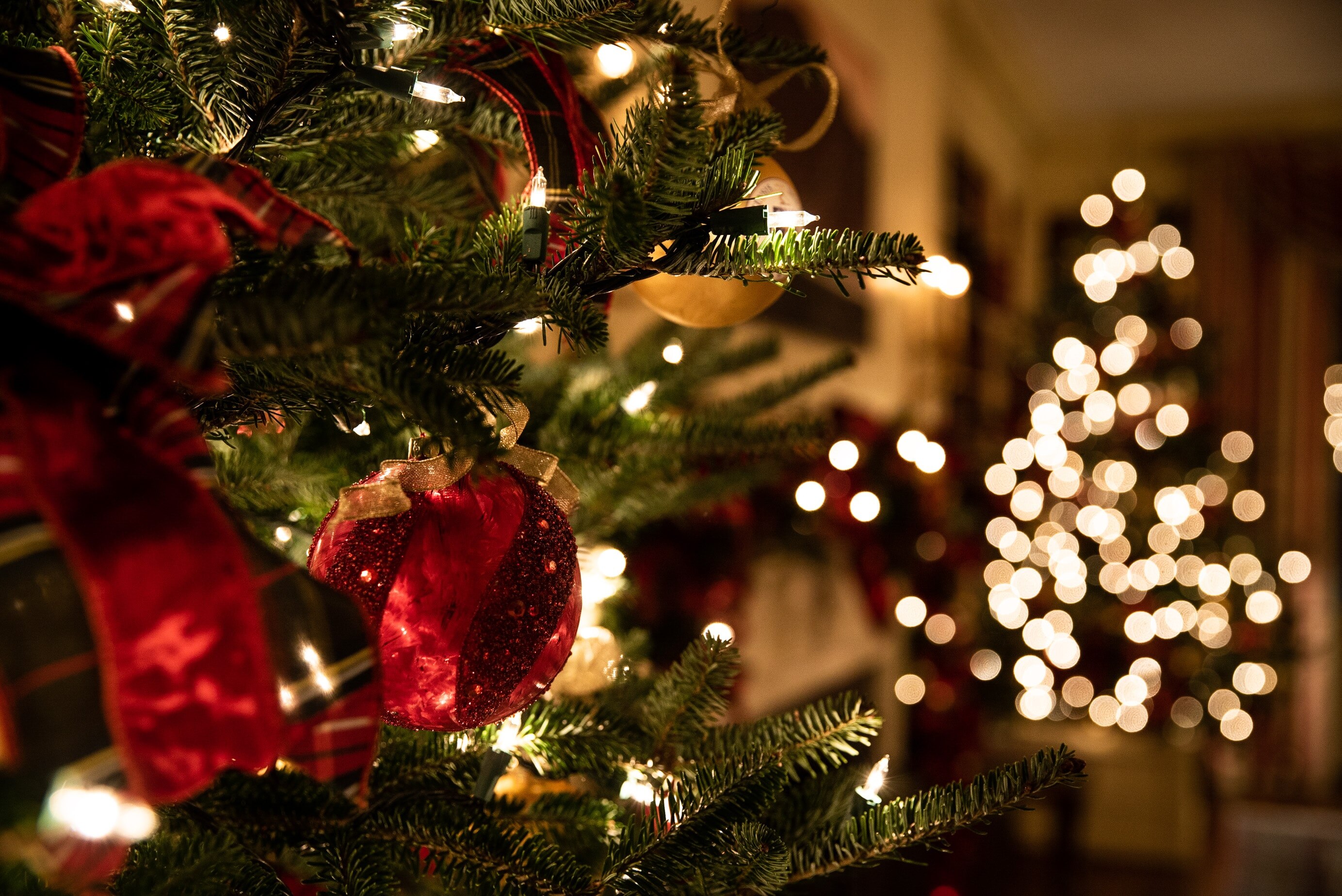 A Christmas tree with lights and red bauble decorations inside someone's house.