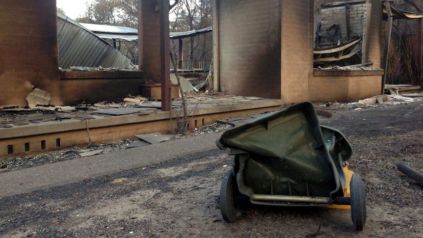 A melted wheelie bin lies on the ground outside a burnt out house after a bushfire tore through Winmalee.