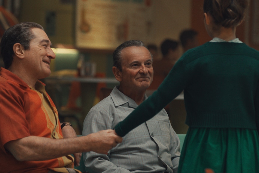 A scene from the Irishman featuring Robert De Nero clasping the hand of a little girl, Joe Pesci in the background