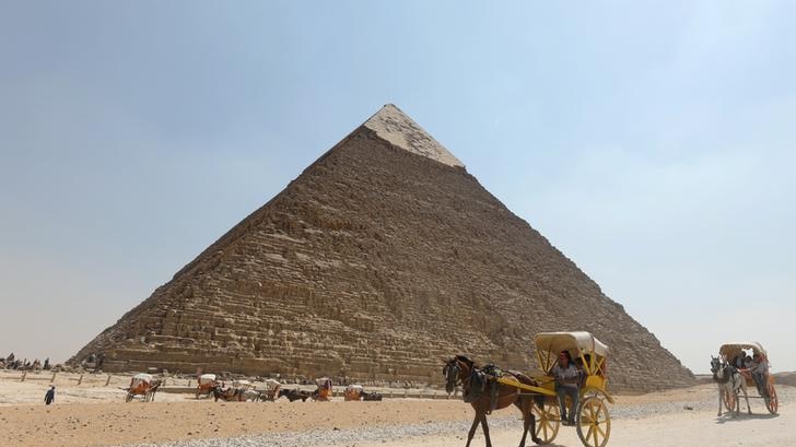 Horse and carts travel in front of a large pyramid